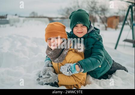 Glückliche Brüder tragen warme Kleidung und spielen im Schnee Stockfoto