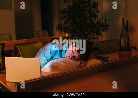 Müder Geschäftsmann, der auf Kissen am Schreibtisch im Büro schläft Stockfoto