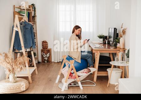 Mutter, die ihr Smartphone benutzt, sitzt im Heimbüro Stockfoto