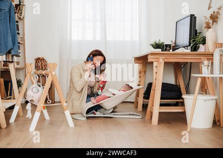 Glückliche Geschäftsfrau, die mit ihrem Smartphone spricht und zu Hause mit ihrer Tochter spielt Stockfoto