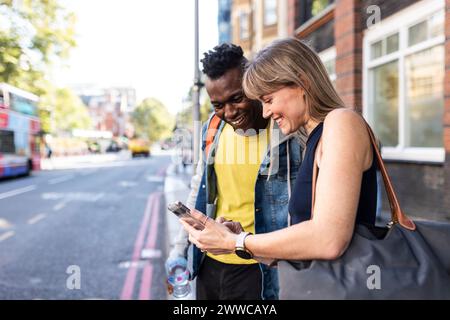 Lächelnde Frau, die ihr Smartphone mit einem Freund teilt, der auf der Straße steht Stockfoto