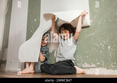 Fröhliche Brüder, die sich zu Hause unter weißer Tapete verstecken Stockfoto