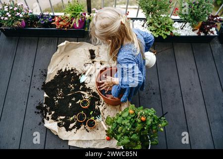 Mädchen mit blonden Haaren, die Dreck mit Füßen im Topf am Balkon tönt Stockfoto