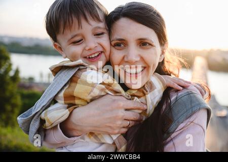 Glückliche Mutter, die den Sohn bei Sonnenuntergang umschließt Stockfoto