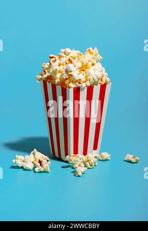 Popcorn in rot gestreiftem Behälter auf blauem Hintergrund Stockfoto