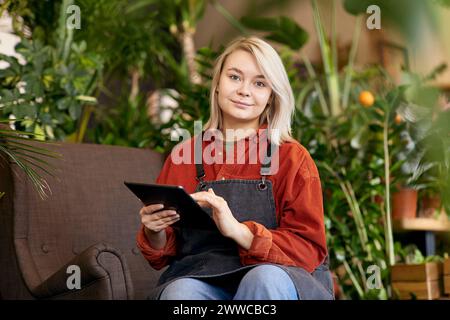 Lächelnder Gärtner sitzt mit Tablet-PC im Geschäft Stockfoto