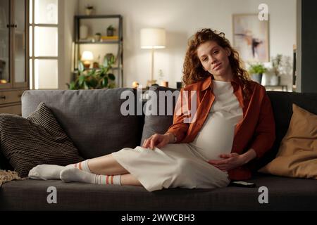 Junge werdende Frau, die im Wohnzimmer auf Sofa sitzt Stockfoto