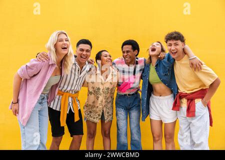 Sorglose Freunde in bunten Kleidern, die mit Armen vor der gelben Wand stehen Stockfoto