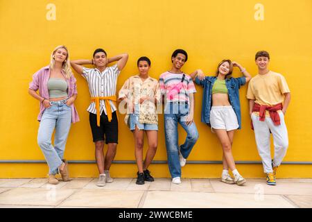 Unbeschwerte Freunde in bunten Kleidern, die an einer gelben Wand hängen Stockfoto