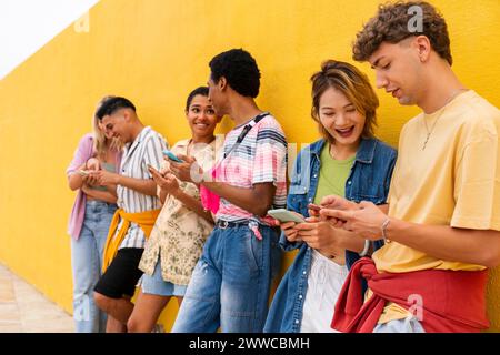 Gruppe von Freunden, die sich mit ihren Smartphones gegen die gelbe Wand lehnen Stockfoto