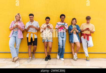 Gruppe von Freunden, die sich mit ihren Smartphones gegen die gelbe Wand lehnen Stockfoto