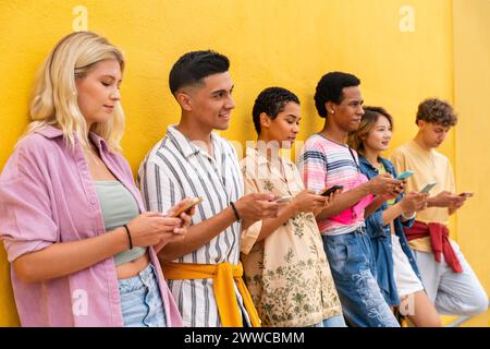 Gruppe von Freunden, die sich mit ihren Smartphones gegen die gelbe Wand lehnen Stockfoto