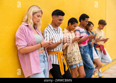 Gruppe von Freunden, die sich mit ihren Smartphones gegen die gelbe Wand lehnen Stockfoto