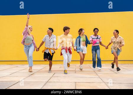 Multi-ethnische Gruppe junger Freunde, die vor der gelben Wand rennen und Hände halten Stockfoto