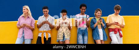 Gruppe von Freunden, die sich mit ihren Smartphones gegen die gelbe Wand lehnen Stockfoto