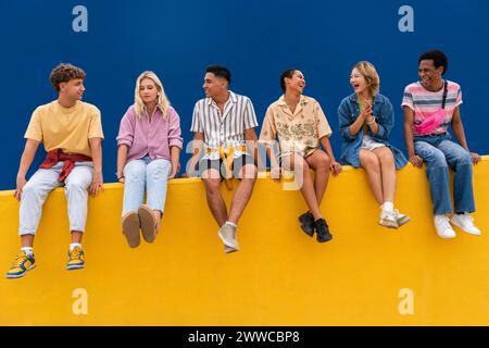 Fröhliche Freunde mit bunten Kleidern sitzen zusammen auf der gelben Wand Stockfoto
