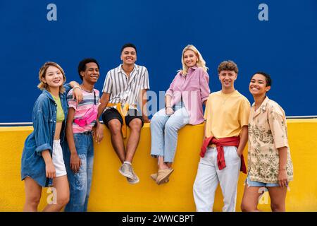 Gruppe von Freunden mit bunten Kleidern, die auf der gelben Wand sitzen und miteinander plaudern Stockfoto