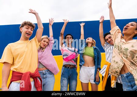 Glückliche Freunde stehen vor der Wand und winken mit erhobenen Armen Stockfoto