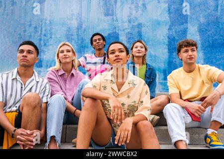 Selbstbewusste junge Menschen, die auf Stufen vor der Wand sitzen Stockfoto