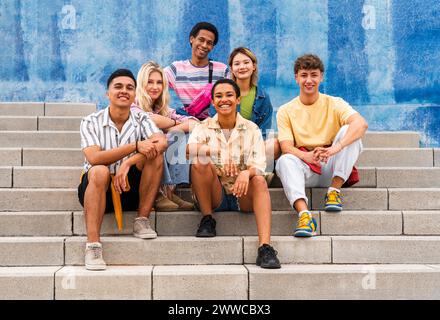 Multiethnische Gruppe junger Menschen, die auf Stufen vor der Wand sitzen Stockfoto