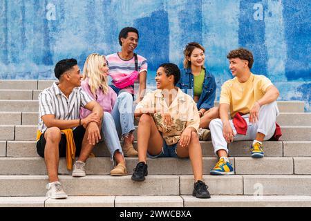 Multiethnische Gruppe junger Menschen, die auf Stufen vor der Wand sitzen Stockfoto