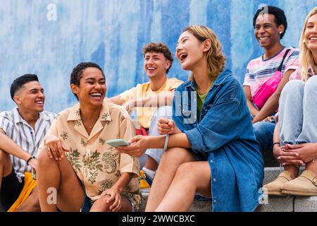 Glückliche Gruppe junger Leute, die auf Stufen vor der Wand lachen Stockfoto