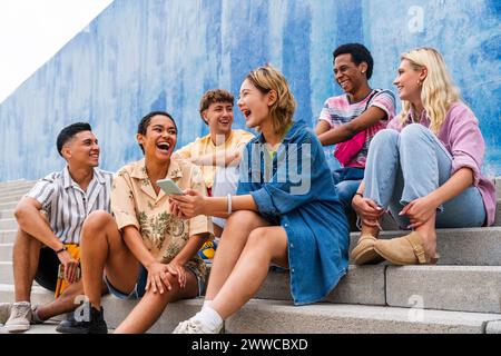 Glückliche Gruppe junger Leute, die auf Stufen vor der Wand lachen Stockfoto