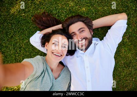 Lächelnde junge Frau, die Selfie mit einem Mann macht, der auf Gras liegt Stockfoto
