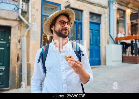 Mann mit traditionellem Dessertpastelll de nata und steht vor dem Gebäude Stockfoto