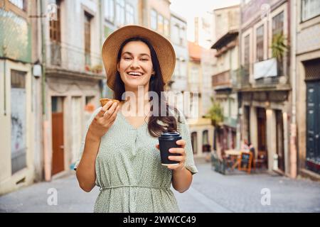 Lächelnde Frau mit Kaffeetasse und traditionellem Dessert Pastell de nata in der Stadt Stockfoto