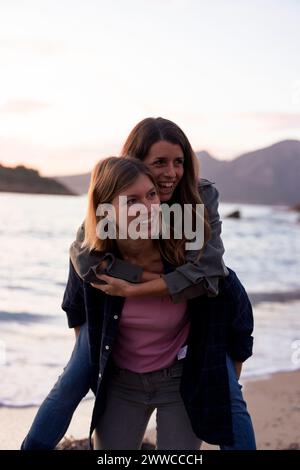 Eine sorglose Frau, die sich mit dem Huckepack befreundet hat, ist am Strand bei Sonnenuntergang Stockfoto