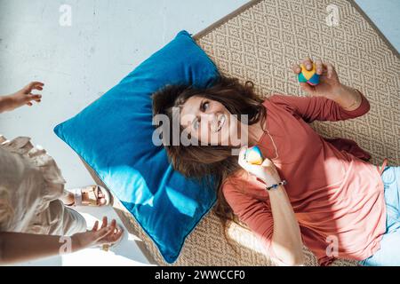 Lächelnde Frau, die Bälle hält und auf der Matte in der Nähe der Tochter zu Hause liegt Stockfoto