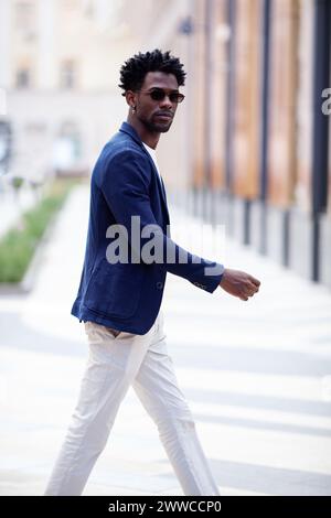 Hübscher, modischer Afroamerikaner geht die Straße hinunter in stilvoller Kleidung, weißer Hose und blauem Blazer. Modischer Street-Style-Trend für Herren. Stockfoto