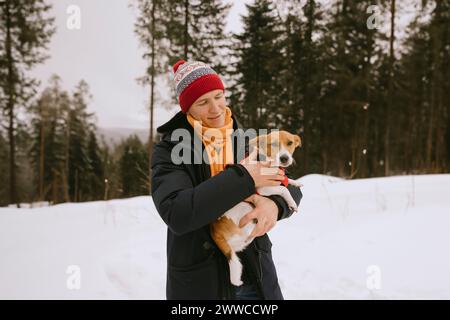 Lächelnder Mann, der Hund im Winterwald hält Stockfoto