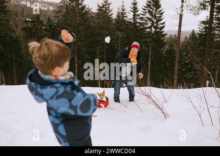 Vater und Sohn spielen mit Schneebällen in der Nähe des Hundes im Winterwald Stockfoto