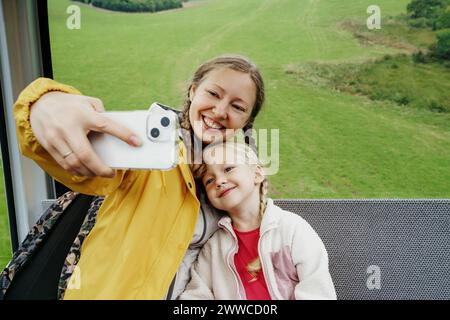 Glückliche Frau, die Selfie mit Tochter macht, über Handy im Skilift Stockfoto