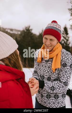 Lächelnder Mann, der die Hände der Frau im Winterwald hält Stockfoto