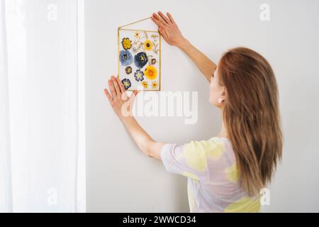 Frau hängender Rahmen dekoriert mit getrockneten Blumen an der Wand zu Hause Stockfoto