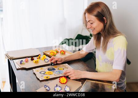 Lächelnde Frau, die zu Hause getrocknete Blumen auf Karton arrangiert Stockfoto