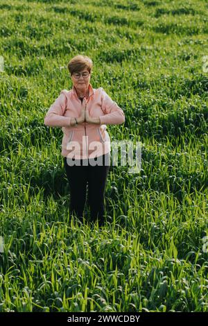 Pensionierte Seniorin, die Yoga auf der Wiese praktiziert Stockfoto