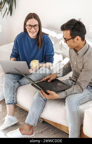 Lächelnde Programmierer mit Laptops, die im kreativen Startup-Büro auf dem Sofa sitzen Stockfoto