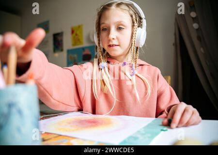 Mädchen mit Kopfhörern und Bleistift vom Tischveranstalter am Tisch Stockfoto