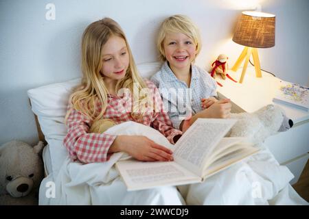 Glückliche Geschwister, die Bücher lesen, sitzen zu Hause auf dem Bett Stockfoto