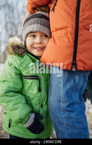 Lächelnder Junge mit Strickmütze, der im Winter mit dem Vater steht Stockfoto