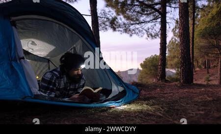 Ein Mann, der bei Sonnenuntergang im Zelt ein Buch liest Stockfoto