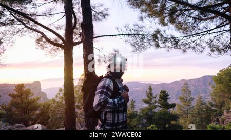 Ein Mann mit Stirnlampe, der neben Bäumen vor Bergen steht Stockfoto