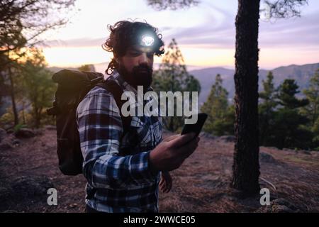 Mann mit Scheinwerfer und Smartphone bei Sonnenuntergang Stockfoto