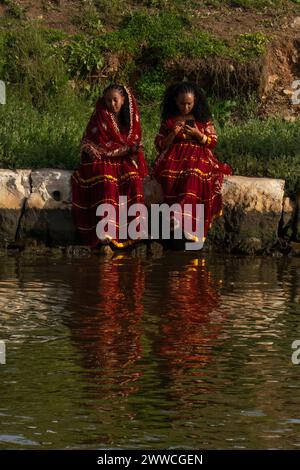 Tel Aviv, Israel - 6. Januar 2023: Zwei Frauen afrikanischer Herkunft, die festliche traditionelle Kleider tragen, sitzen am Ufer des Yarkon. Stockfoto