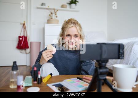 Bild einer jungen Frau, Vlogger nimmt Video auf Digitalkamera auf, zeigt Schönheitsprodukte, empfiehlt Make-up für das Publikum in sozialen Medien, sitzt vorne Stockfoto