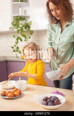 Mutter und Tochter kochen Kuchen in lila Küche, Training und Entwicklung, interessantes Spiel und Hilfe. Glückliche Familie zusammen. Lächeln Stockfoto
